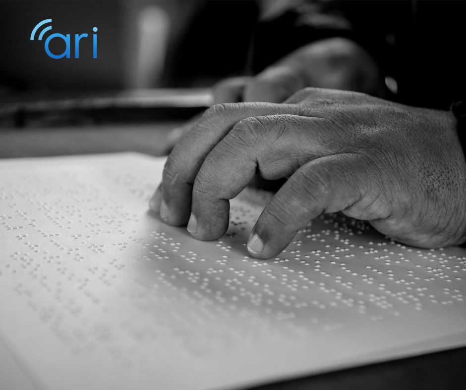 Close up black and white image of a person’s hand reading Braille text on a sheet of embossed paper, with focus on the fingertips touching raised dots.