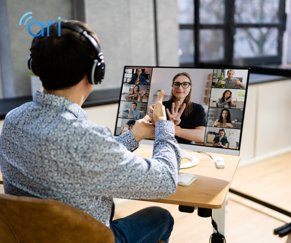 Person wearing headphones sits at a desk participating in a video conference where multiple participants are communicating using sign language on screen.