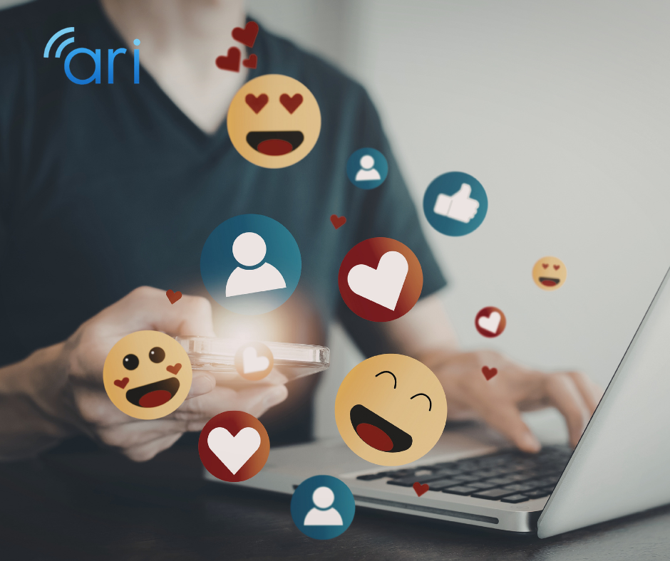 Person using a smartphone and laptop with floating social media reaction icons, representing online engagement and digital communication platforms.