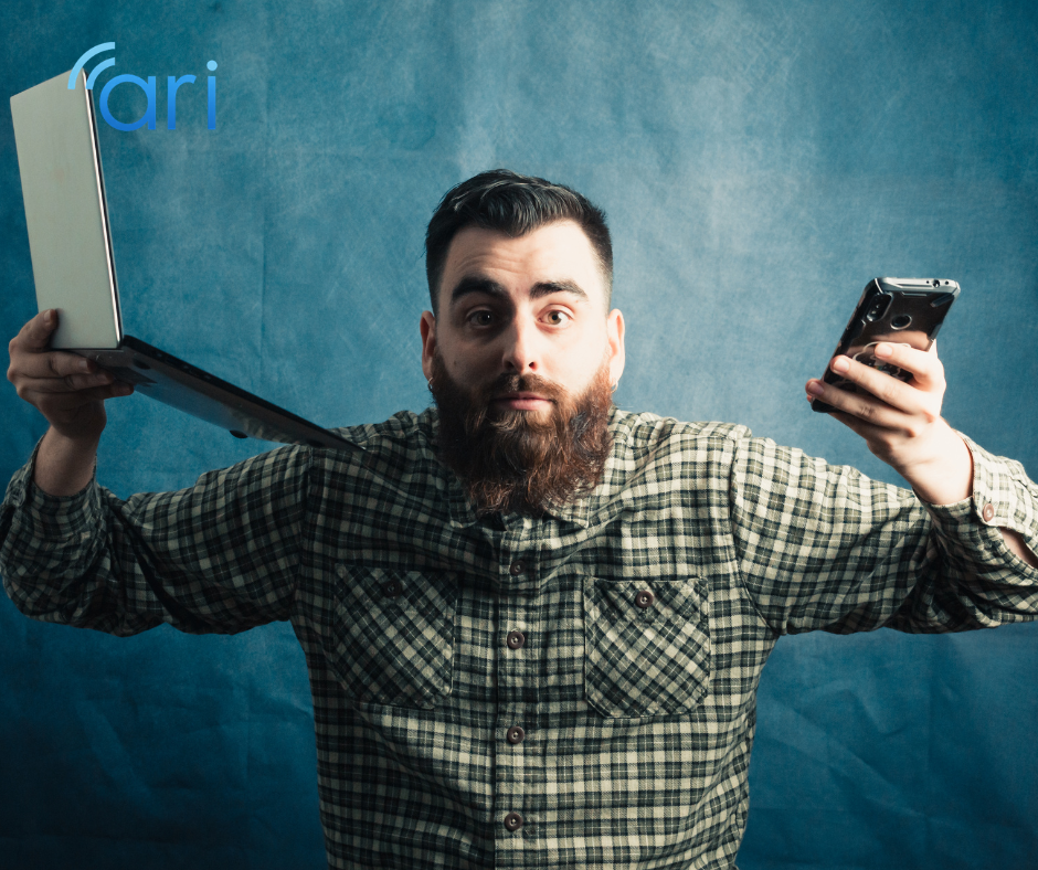 Man holding a laptop in one hand and a smartphone in the other, illustrating the complexity of managing communication across multiple digital and social media platforms.