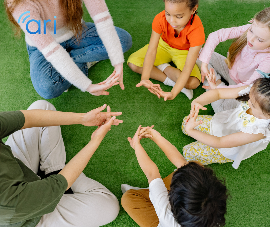 Teacher and young children sitting in a circle using hand gestures during a group activity designed to support inclusive communication for children with hearing loss.